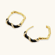 Small gold-plated hoop earrings with black enamel stripes and cubic zirconia crystals on white background.