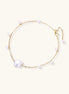 Delicate gold chain bracelet with baroque pearl centerpiece and small freshwater pearls on cream background.