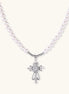 White pearl necklace with ornate silver cross pendant featuring zirconia crystals on cream background.
