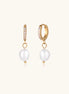 Gold huggie hoop earrings with pavé crystals and white freshwater pearl drops on cream background