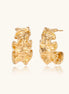 Pair of gold huggie hoops with sculpted wave texture and dimensional ripples on neutral background.