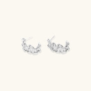 Textured white gold-plated hoop earrings with flowing wave pattern against cream background, showing dimensional rippled surface.