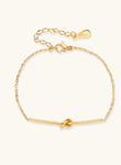 Delicate gold chain bracelet with minimalist bar and centered knot detail on cream background