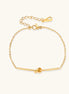 Delicate gold chain bracelet with minimalist bar and centered knot detail on cream background