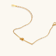 Delicate gold chain bracelet with minimalist bar and centered knot detail on cream background