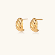Chunky gold twisted rope huggie hoops with diagonal grooves and high-polish finish on cream background