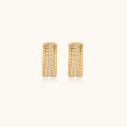 Textured gold huggie hoop earrings with raised ribbed rows creating dimensional sculptural design on cream background
