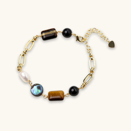 Gold chain bracelet with tiger's eye, obsidian, pearl, and iridescent abalone stones on cream background.